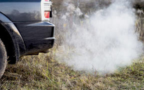 The back of the black car with the emission of smoke from the exhaust pipe on the background of nature. The concept of environmental pollution by vehicles.