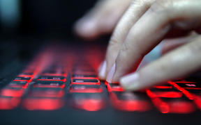 Teenage Hacker Girl Attacks Corporate Servers in Dark, Typing on Red Lit Laptop Keyboard. Room is Dark