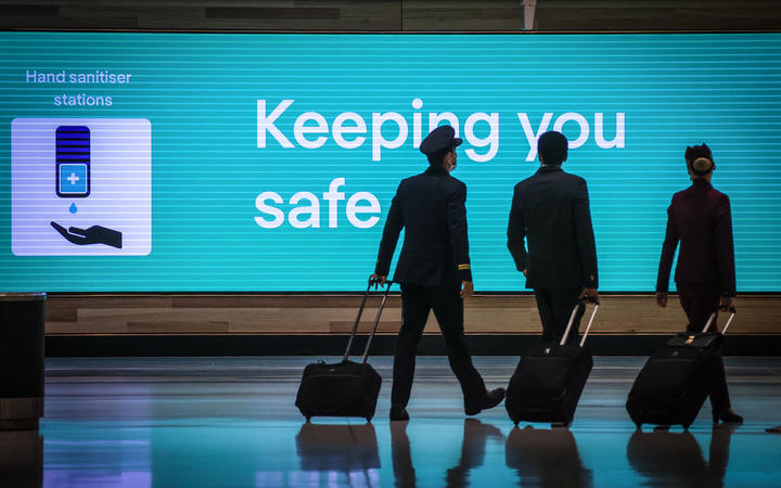 Des membres d'équipage de conduite de Qatar Airlines passent devant un panneau lumineux affichant un message concernant le nouveau coronavirus Covid-19 à l'aéroport international de Sydney à Sydney, en octobre 2020.