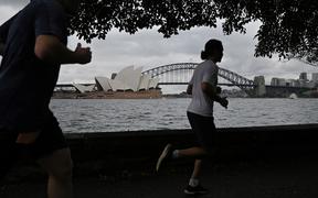 People run before the Opera House and Harbour Bridge in Sydney on December 20, 2020, after authorities introduced a fresh round of restrictions.