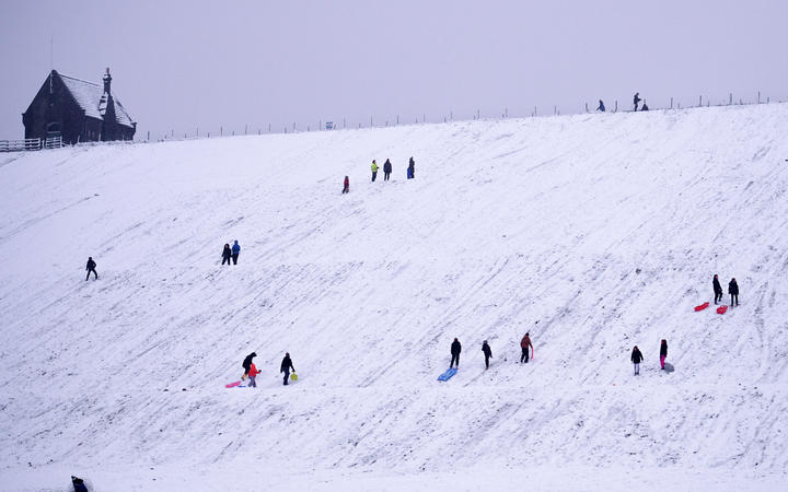 People sledge down a hillside at  Butterley Reservoir in Marsden, northern England on January 14, 2021 as heavy snow fell on parts of the UK