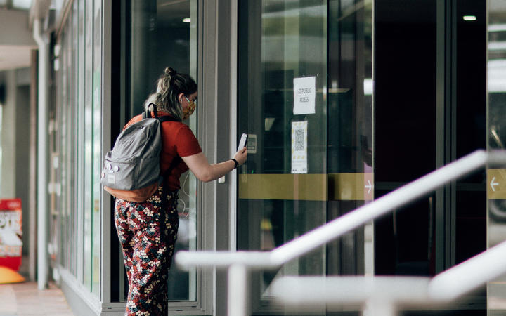 A woman using the Covid Tracer app at a QR code in the window of a business during level 2 in Wellington on15 February 2021