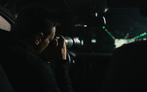 A generic photo of a man in his car doing surveillance with a camera.