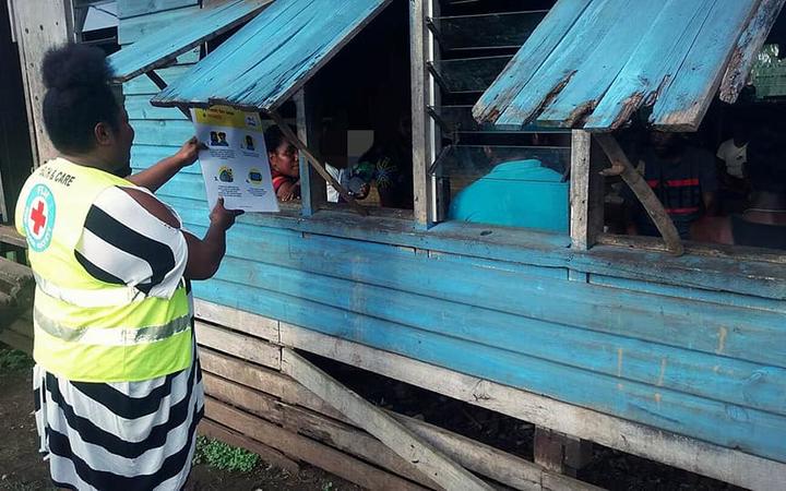 A Red Cross volunteer shares a message about Covid-19 transmissions through a window to a family in Uciwai Settlement, Nadi.