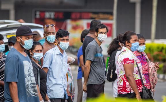 This picture taken on April 24, 2021 shows residents wearing face masks waiting to cross the main road in the Fijian capital Suva ahead of an expected lockdown in the capital due to a Covid-19 spike. (Photo by Leon LORD / AFP)