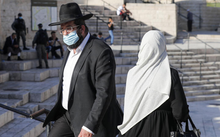 A Palestinian woman and a religious Jewish man walk past each other at the Damascus Gate of the old city of Jerusalem, on May 31, 2020. 