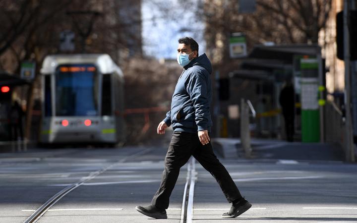 A man crosses an empty street in Melbourne on 23 August 2021, as the city experiences its sixth lockdown while battling an outbreak of the Delta variant of coronavirus. 