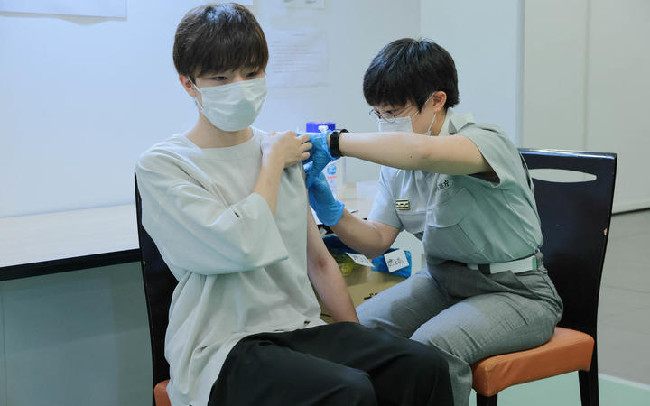 A Tokyo fire brigade staff member (R) administers a dose of the Covid-19 coronavirus vaccine at Aoyama University in Tokyo on August 2, 2021. 