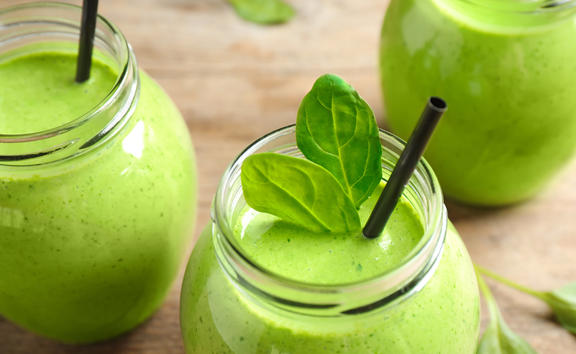 Jars of healthy green smoothie with fresh spinach on wooden table, closeup view