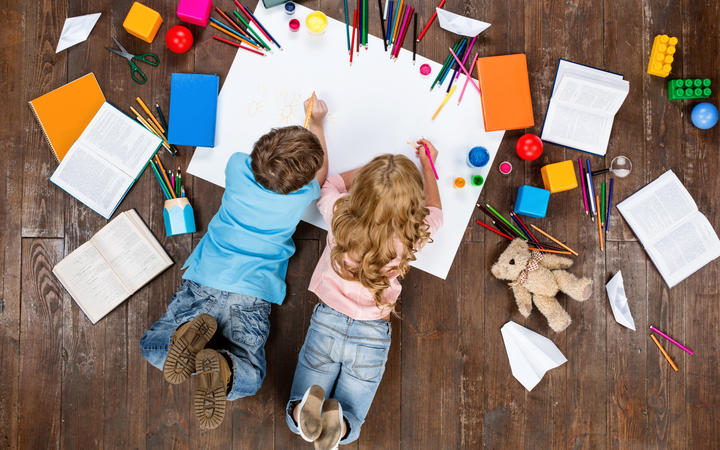 Happy baby Top view creative photo of little boy and girl on vintage brown wood floor. The children are lying near books and toys and paintings.