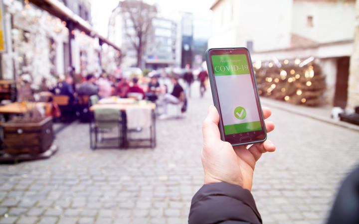 Vaccinated person using a digital vaccination or immunisation certificate on a smartphone at a restaurant terrace.