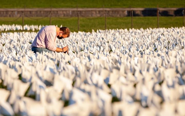 A person kneels to take photos of some of the more than 670,000 white flags covering 20 acres of the National Mall in an art memorial for Covid-19 victims by Suzanne Brennan Firstenberg In America: Remember. 