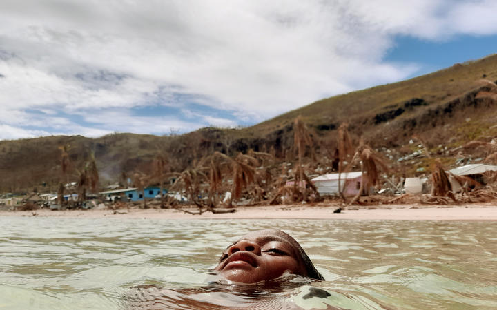 Ten year old Epineri Lata takes a dip in the ocean to escape the intense heat on the island of Kia in Fiji. In the background is the visible evidence of cyclone damage to the island.