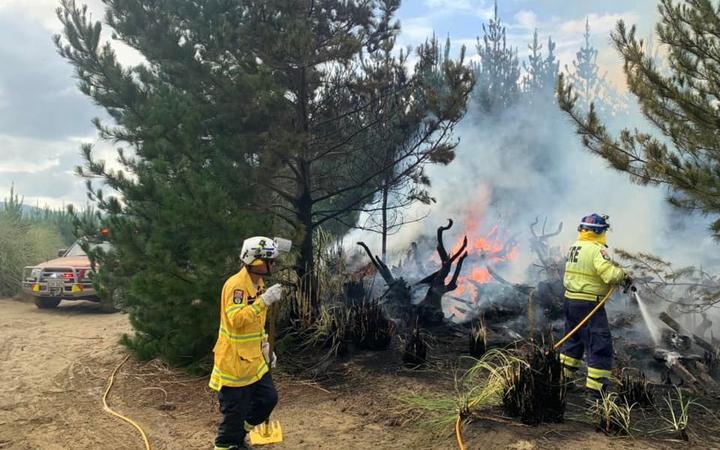 Muriwai Volunteer Fire Brigade firefighters tackling a forest fire which started from a campfire at Muriwai Beach.