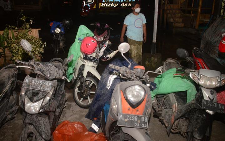 A villager walks past the motorbikes of evacuees covered by volcanic ashes at Sumberurip village, in Lumajang, on December 4, 2021, after the Semeru volcano eruption. 