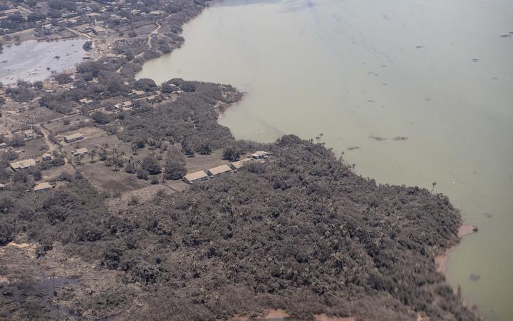 A P-3K2 Orion aircraft flies over an area of Tonga that shows Ash on homes and surrounding vegetation.