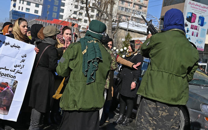 Taliban fighters trying to control women as they chant slogans during a protest demanding for equal rights, along a road in Kabul on 16 December, 2021. 