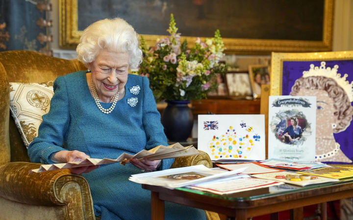 2022 年 1 月，英国女王伊丽莎白二世在伦敦西部温莎城堡的橡树厅里看着维多利亚女王的签名扇，旁边展示了她的金禧和白金禧年的纪念品。