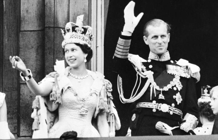 1953 年 6 月 2 日，在伦敦威斯敏特教堂加冕后，英国女王伊丽莎白二世 (左) 在英国爱丁堡公爵菲利普亲王 (右) 的陪同下向人群挥手致意。