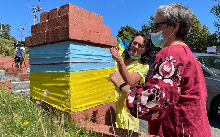 Tetiana Zhurba (left) and Nataliya Stepuroi put the colours of the Ukranian flag around a brick post by the embassy's driveway.