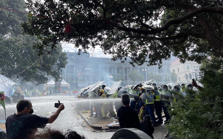Police using hoses on the fire from behind riot shields.