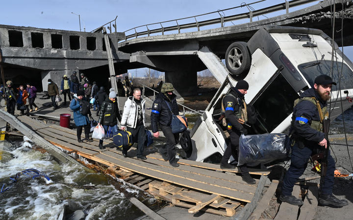 Ukrainian police officers help residents to cross a destroyed bridge as they evacuate Irpin, northwest of Kyiv, on 12 March 2022. 