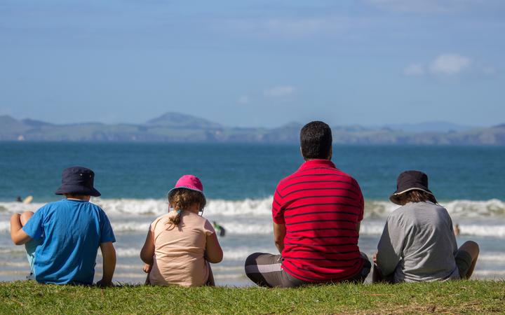 父亲和三个孩子坐在新西兰北部的马陶里湾海滩观看海浪