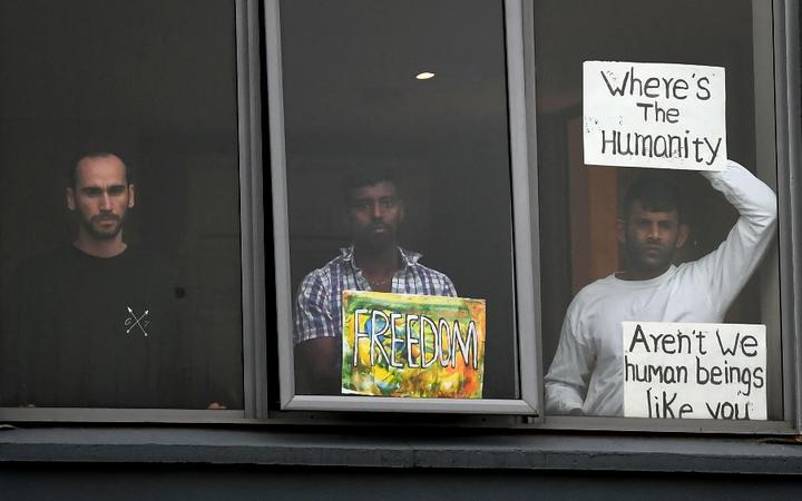 Three asylum seekers gesture to protesters holding a pro-refugee rights rally from their hotel room where they have been detained in Melbourne on June 13, 2020, after they were evacuated to Australia for medical reasons from offshore detention centres on Nauru and Manus Island.