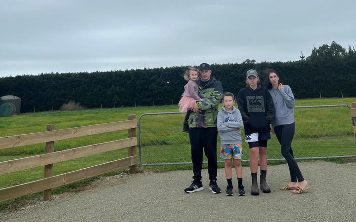 The Stockers - Poppy, Brad, Robbie, Dean, and Ellie, stand at the entrance to where their home would be by now, if not for an ongoing hold up around wastewater consents.