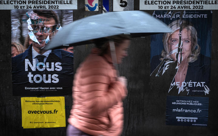 A pedestrian walks past campaign poster of French President Emmanuel Macron and presidential candidate Marine Le Pen of the far-right Rassemblement National party.