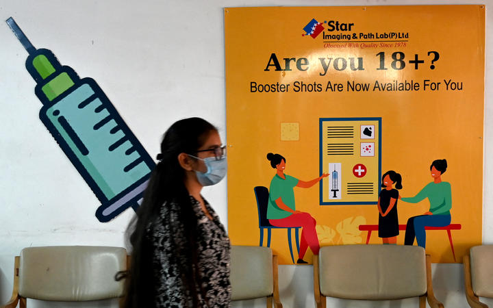 A girl walks past a poster at a vaccination centre in New Delhi on April 10, 2022, after government announced the paid precaution dose against Covid-19 coronavirus to be available for everyone above 18 years of age at private vaccination centres. 