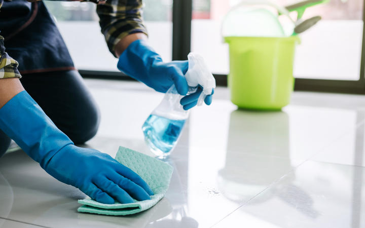 Husband housekeeping and cleaning concept, Happy young man in blue rubber gloves wiping dust using a spray and a duster while cleaning on floor at home.