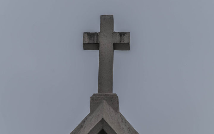 Catholic church steeple with cross on top, sky as background.