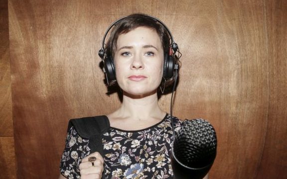 A portrait of Bang! presenter Melody Thomas, thrusting a microphone towards the camera.