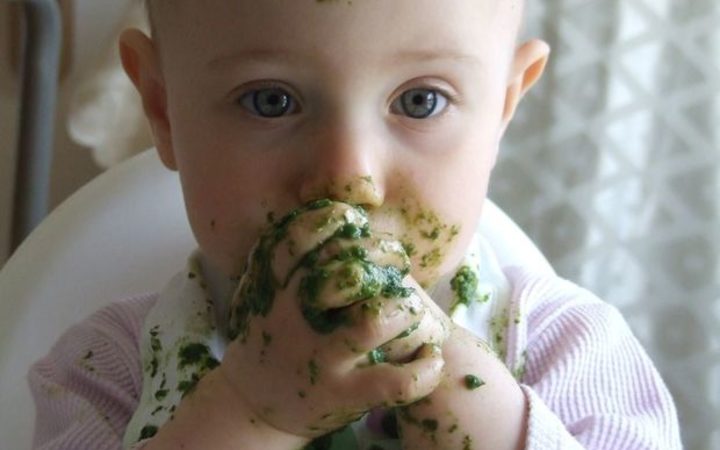 A photo of a toddler eating messy green food with her fingers