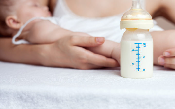 A mother holds a baby next to a bottle of milk. 