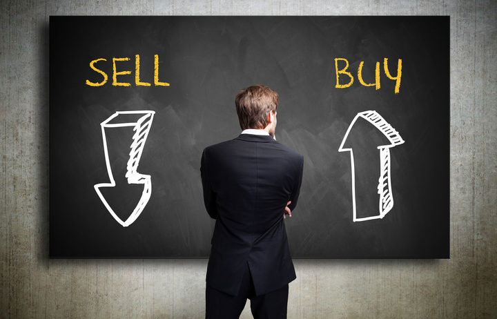 Businessman standing in front of a blackboard trying to decide whether to buy or to sell