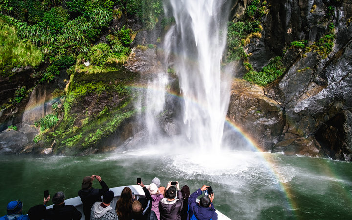 A group of tourists enjoying a stunning scene of nature while cruising into waterfall in Milford Sound, New Zealand.