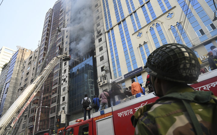 A Bangladehi Army stnad guard as Bangladeshi firefighters on ladders work to extinguish a blaze in Dhaka.
