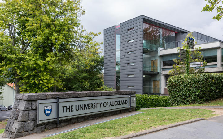 Auckland, New Zealand - March 1, 2017: Sign and logo of University of Auckland set near modern dark gray offices in green park like environment. Gray sky.