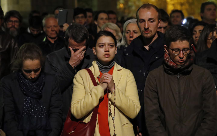 People pray as Notre Dame cathedral burns.