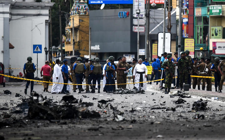 Sri Lankan security personnel inspect the debris of a car after it explodes when police tried to defuse a bomb near St. Anthony's Shrine as priests look on in Colombo on April 22, 2019, a day after the series of bomb blasts targeting churches and luxury hotels in Sri Lanka. 