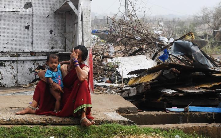 An Indian woman sits with her child next to storm-damaged buildings in Puri in the eastern Indian state of Odisha,