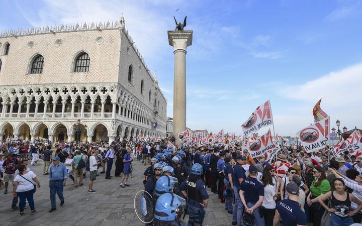 
Police officers face people holding flags as they arrive close to San Marco square during a demonstration called by the No Great Ships movement against big cruise ships sailing into the Venice.
