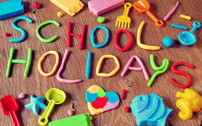the text school holidays made from modelling clay of different colors and some beach toys such as toy shovels and sand moulds, on a rustic wooden surface