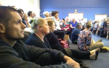 Paul Chronis and Charlotte Boocock sit on the church hall floor at a packed Island Bay meeting.