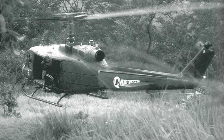 An RNZAF Iroquois hovering just above the ground as it waits to pick up a patrol in the Tilomar area. The door gunner, LAC Daryl Fell, is checking the tail rotor clearance; March 2000.

