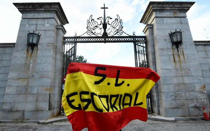 A man holds a Spanish flag in front of the closed access road to the Valle de los Caidos (The Valley of the Fallen), a monument to the Francoist combatants who died during the Spanish civil war and Franco's final resting place.