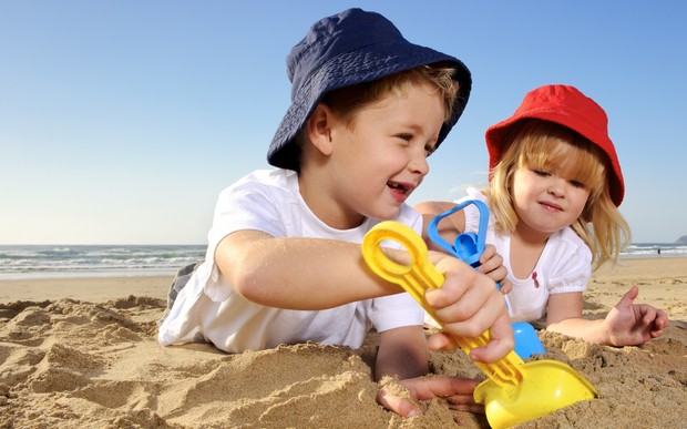 Two children wearing hats play with spades on a sunny day at the beach. 