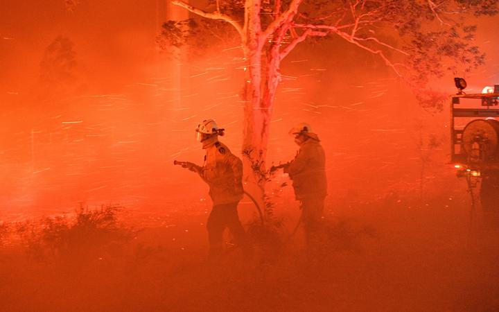 Firefighters struggling against strong winds and flying embers in an effort to secure nearby houses from bushfires near the town of Nowra in the Australian state of New South Wales on 31 December.
